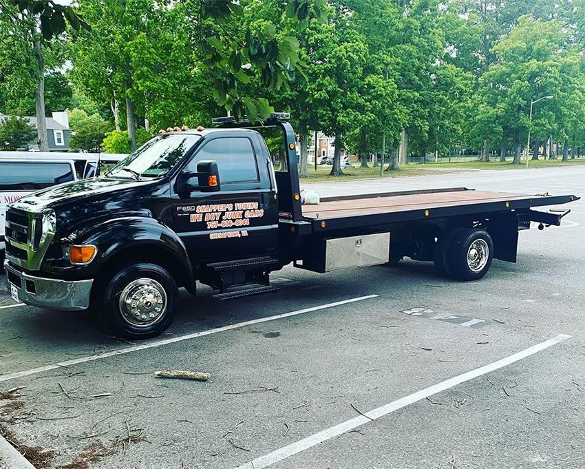 Black flatbed tow truck parked in a lot, trees in the background.