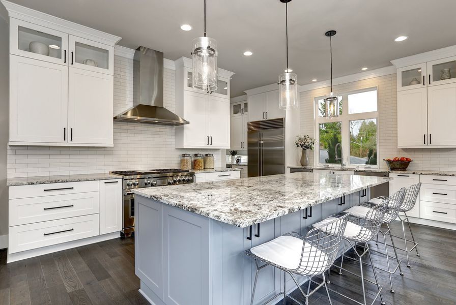 Modern kitchen with white cabinets, gray island, stainless steel appliances, and wood flooring.