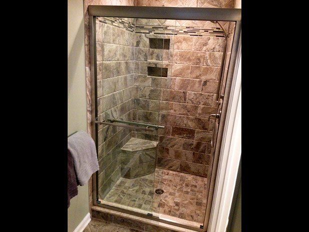 Shower stall with tile walls, glass door, and built-in bench.