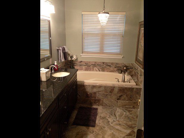Bathroom with bathtub and vanity; green wall, dark cabinets, stone tub surround, crystal chandelier.