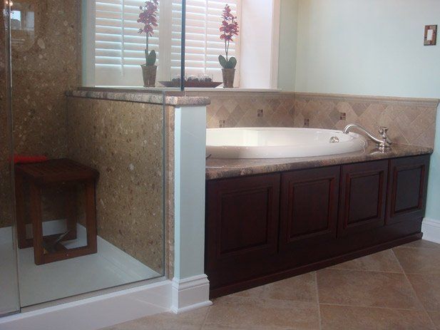 Bathroom with dark wood cabinetry, a built-in tub, and a shower with stone tile accents.