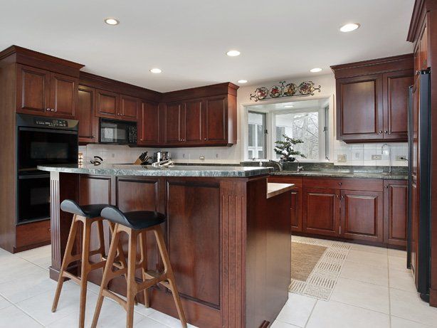 Kitchen with dark wood cabinets, island with stools, and green countertop.