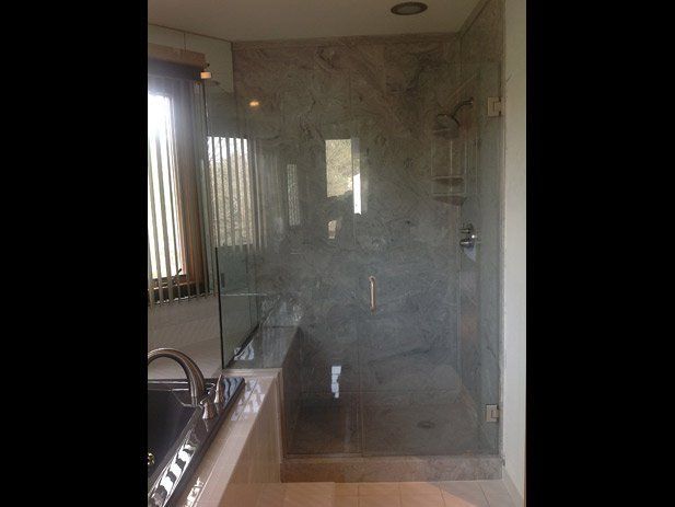 Glass shower enclosure next to a window, marble walls, and a tiled floor.