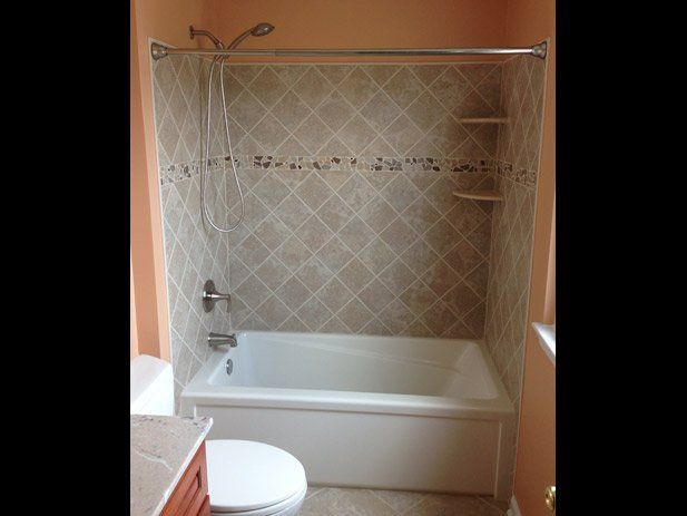 Bathroom with white tub, beige tile backsplash, showerhead, and orange walls.