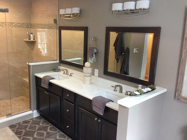 Bathroom with a double vanity. Dark wood cabinets, white countertops, two mirrors, and a shower with glass doors.