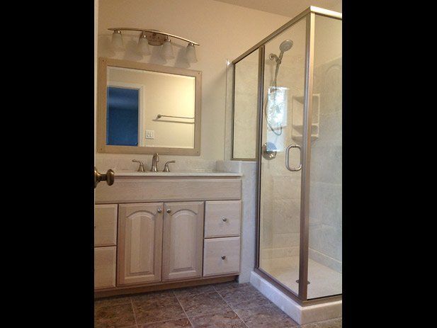 Bathroom with a beige vanity, mirror, shower, and tan tile floor.