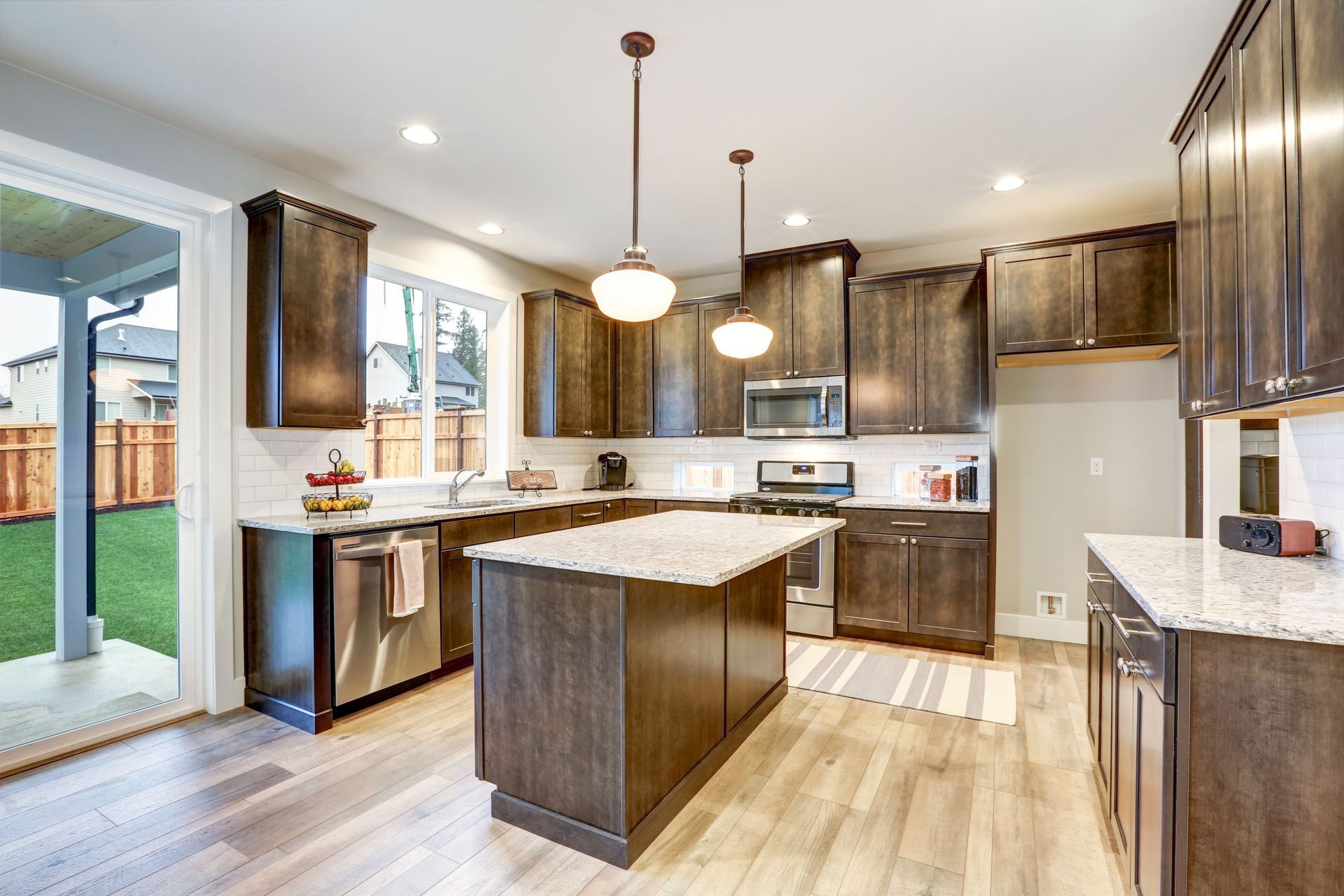 Modern kitchen with brown cabinets, island, and granite countertops; view of outdoor patio.