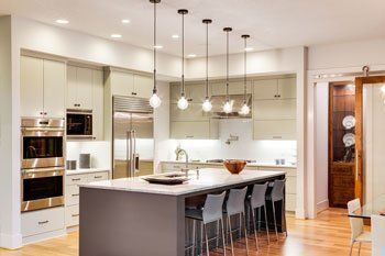 Modern kitchen with a gray island, pendant lights, stainless steel appliances, and wood floors.