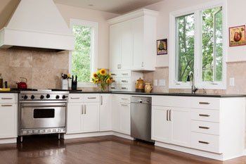 White kitchen with stainless steel appliances, windows, and dark countertops.