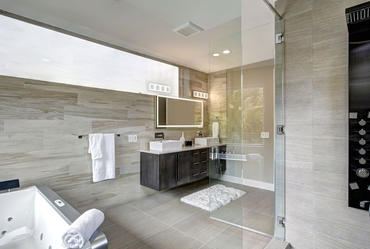 Modern bathroom with gray tiled walls, glass shower, tub, and floating vanity.