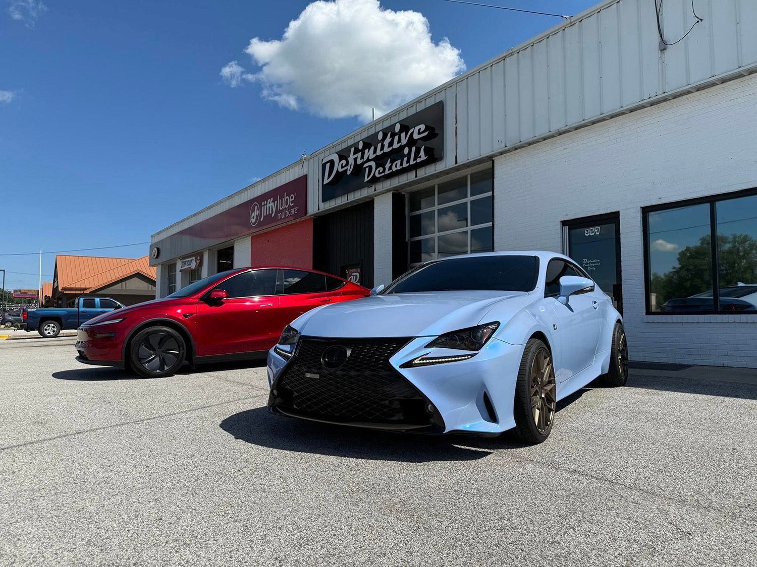 Light blue Lexus and red Tesla parked outside a business called 