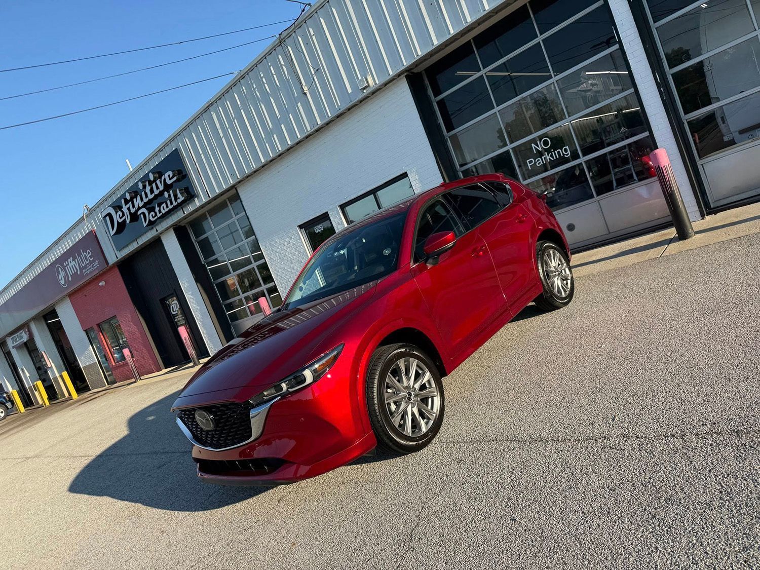 Red Mazda hatchback parked in front of a building with a garage door.