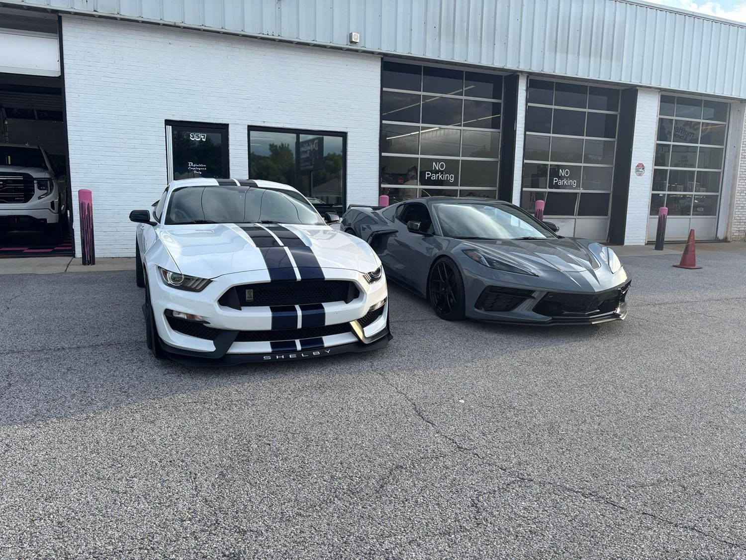 White Ford Mustang with blue stripes and gray Chevrolet Corvette parked in front of a building.