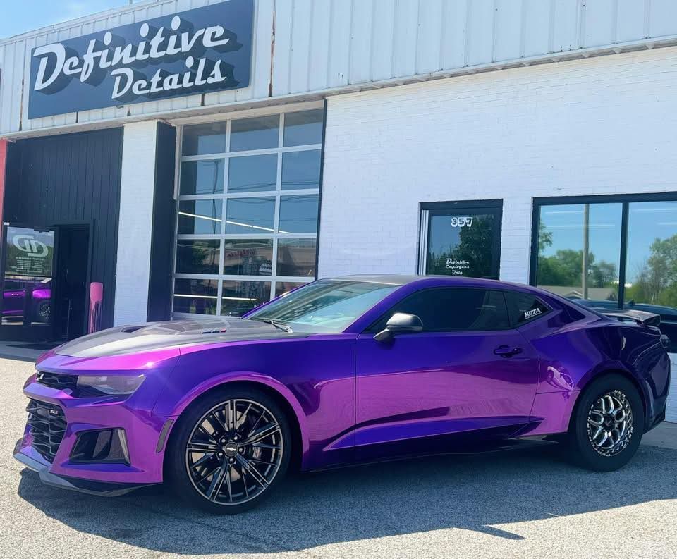 Purple Camaro car parked outside a shop called Definitive Details.
