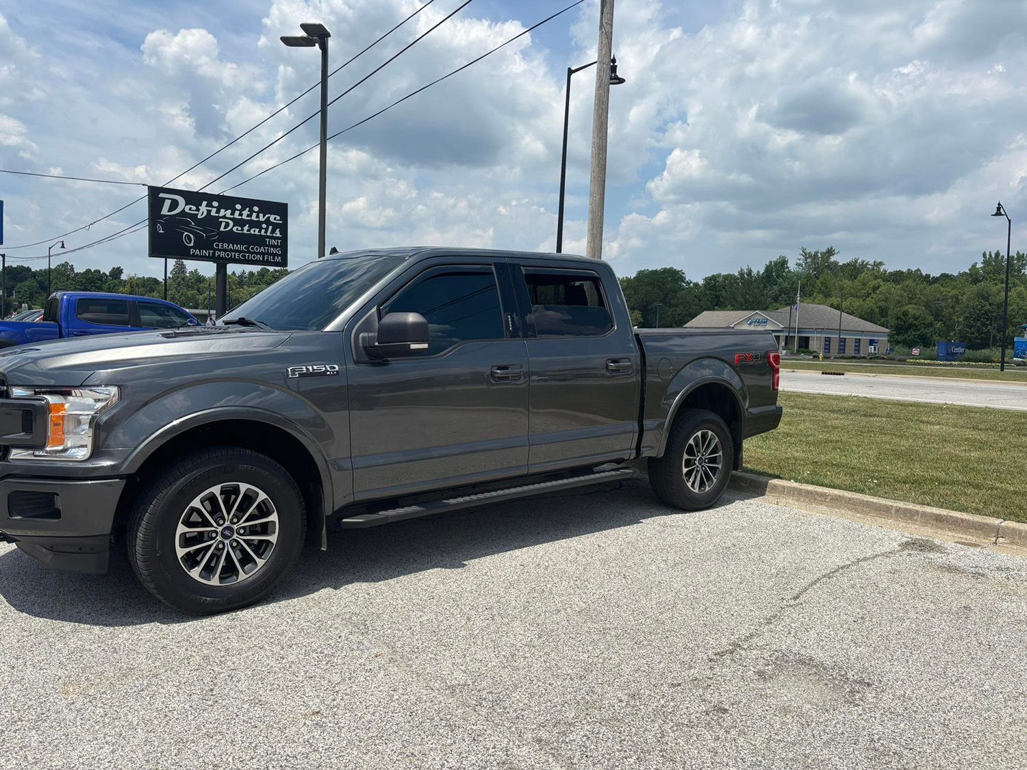 Gray Ford F-150 pickup truck parked on gravel. Cloudy sky in the background, daytime.