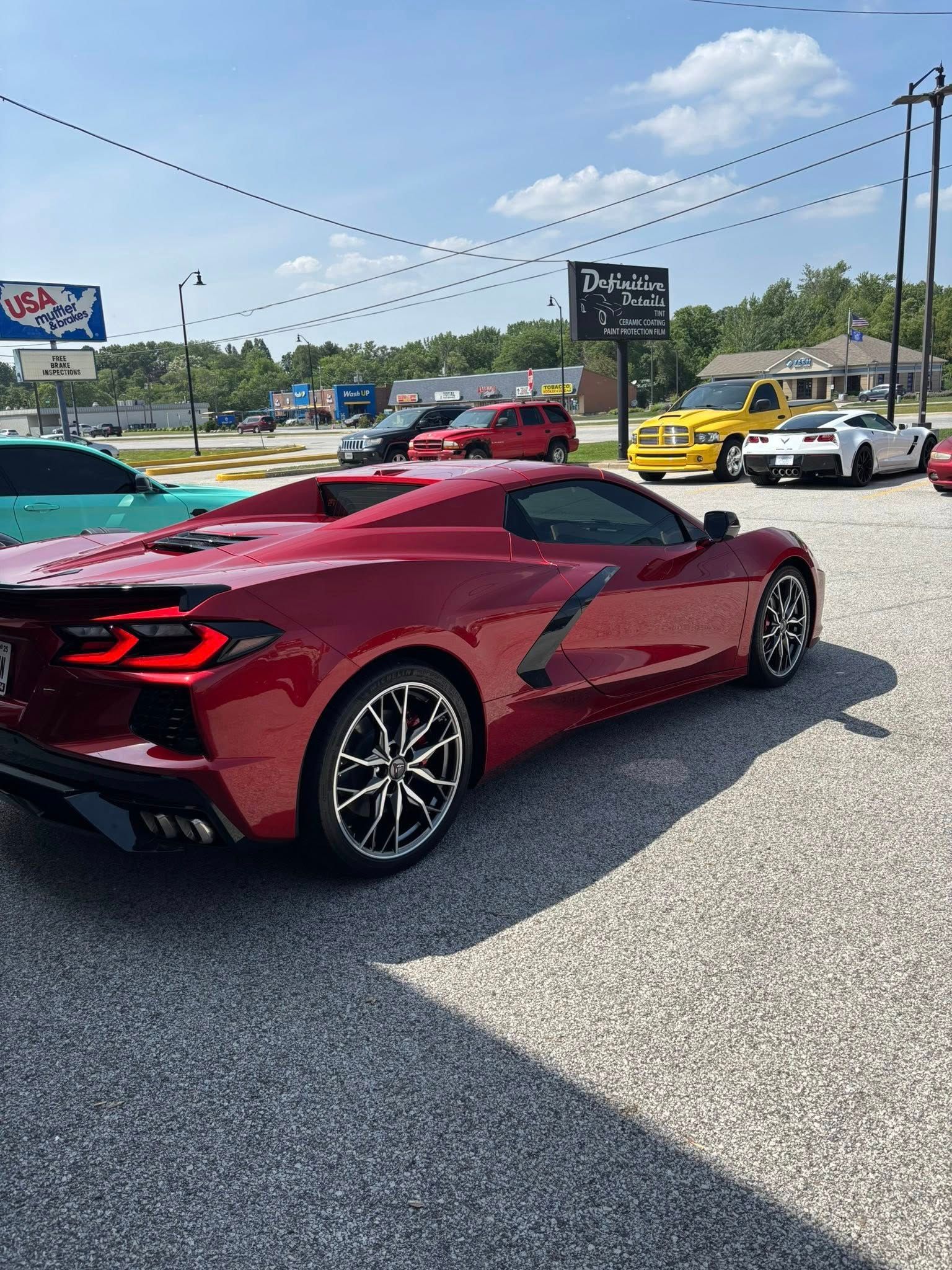 Red Corvette sports car parked on asphalt, other cars in background, sunny day.