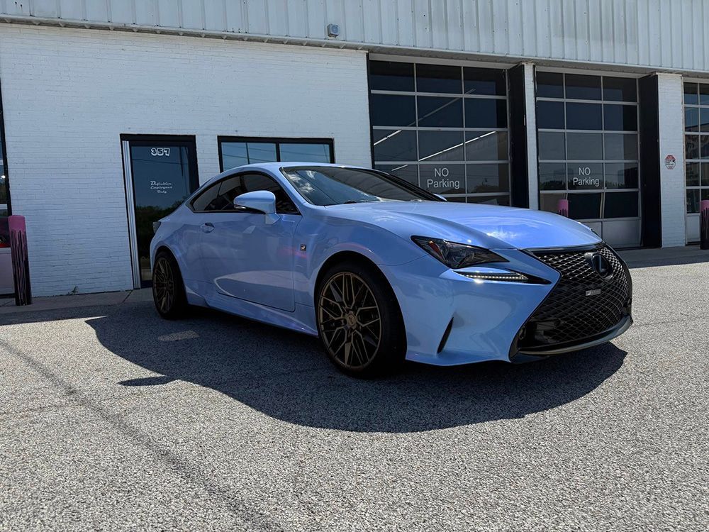 Blue Lexus RC coupe parked in front of a white building with garage doors.