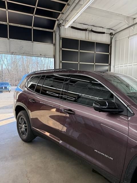 A burgundy SUV parked in a garage with tinted windows. The open garage door reveals trees.