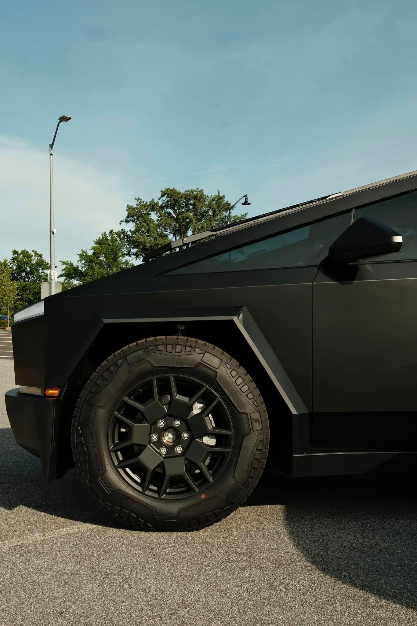 Black Tesla Cybertruck with black wheels on asphalt road under blue sky.
