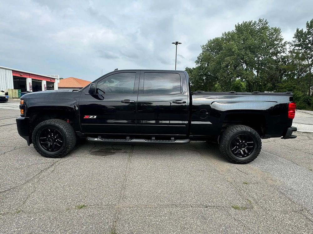 Black Chevrolet pickup truck on asphalt, black wheels, under cloudy sky.