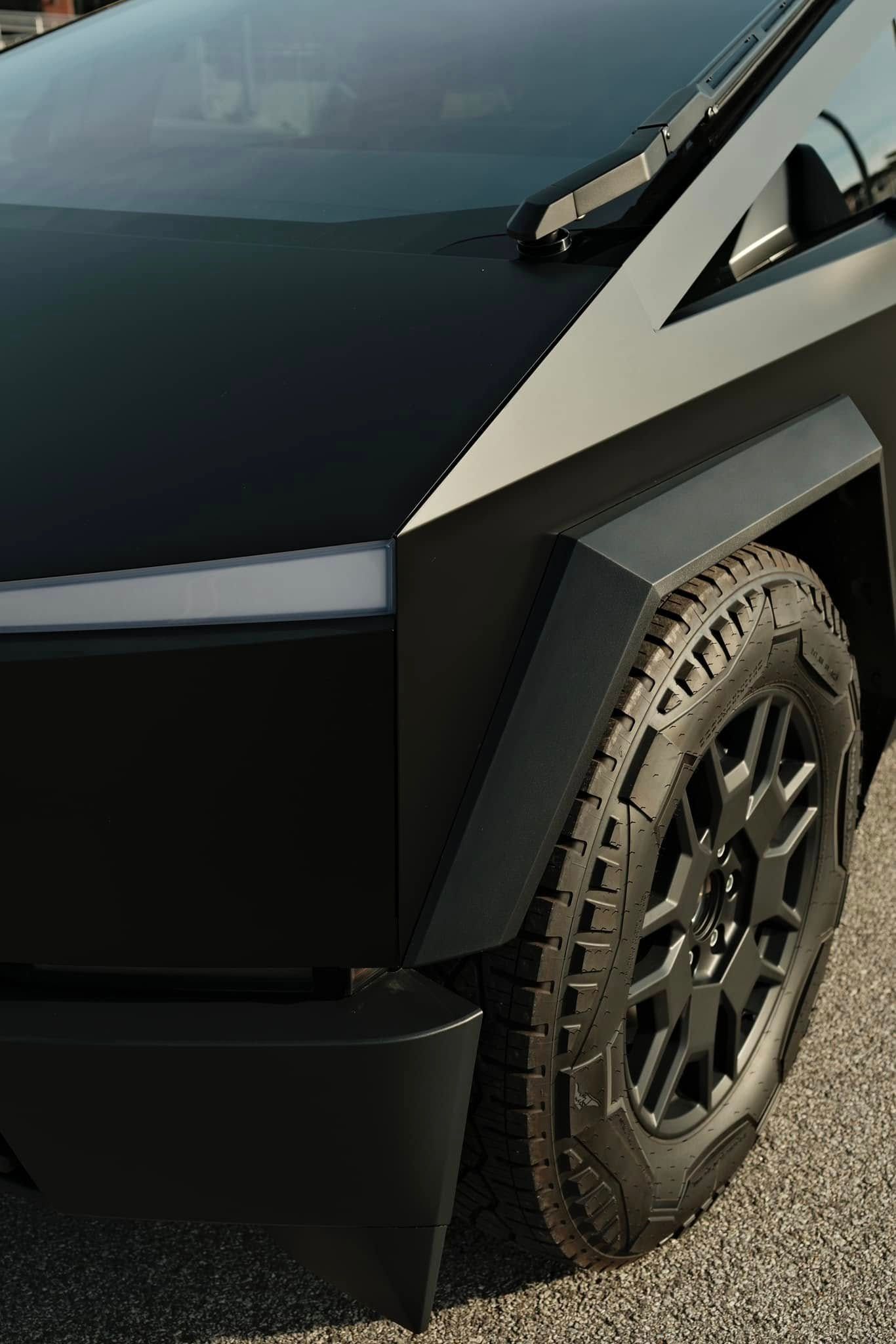 Black Tesla Cybertruck's front quarter showing the geometric design, black tires, and a dark, matte finish.