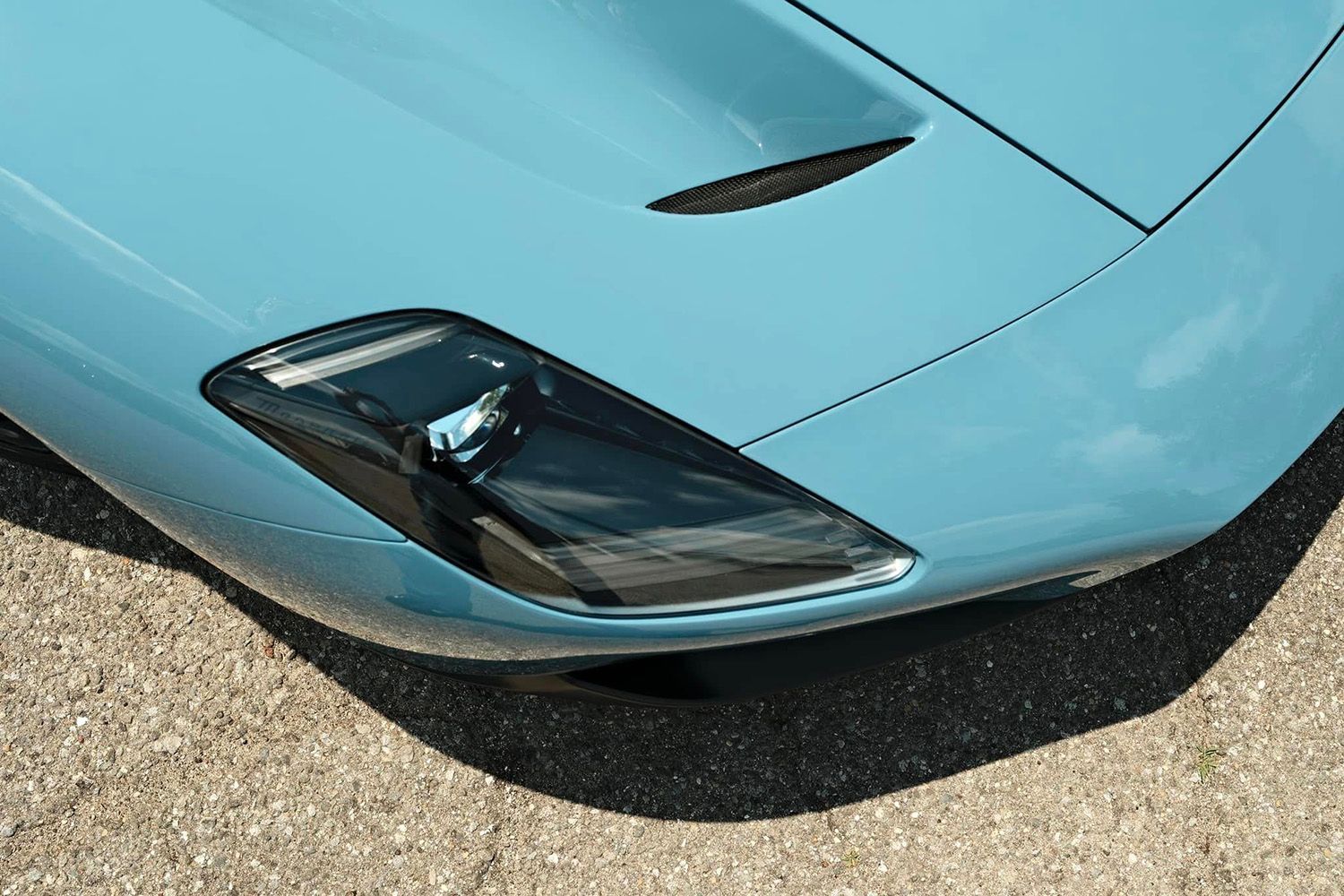 Close-up of a teal-colored sports car's front with a black headlight and a hood vent.