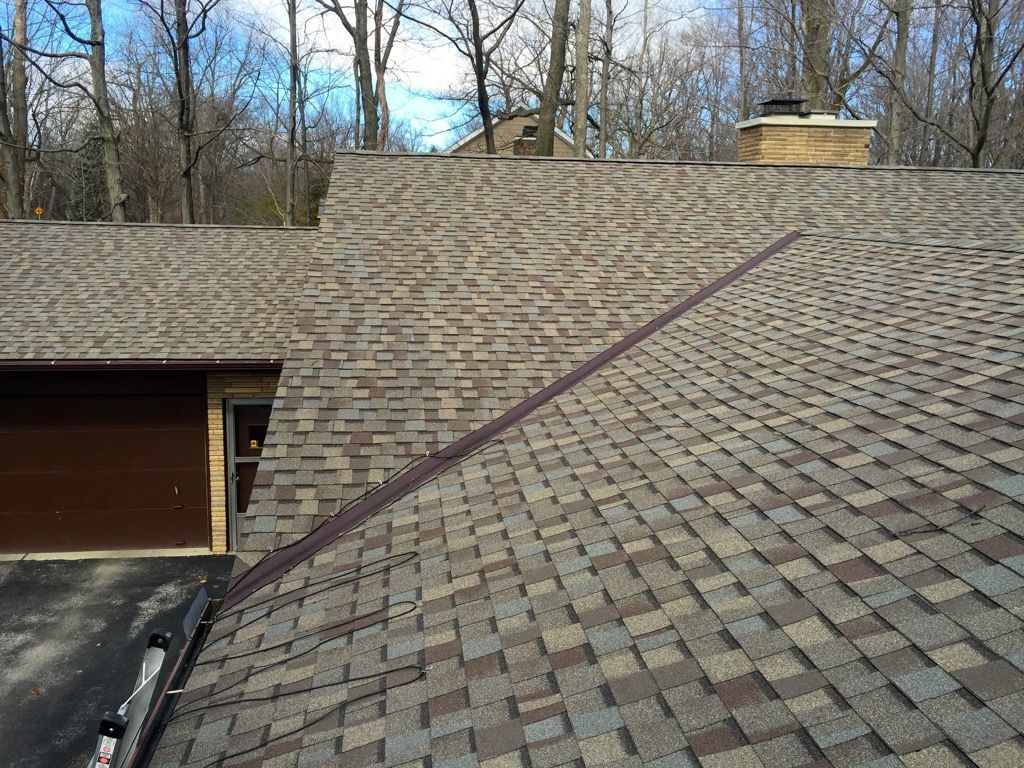 Residential roof with asphalt shingles and a dark roofline stripe, viewed from above near a garage.