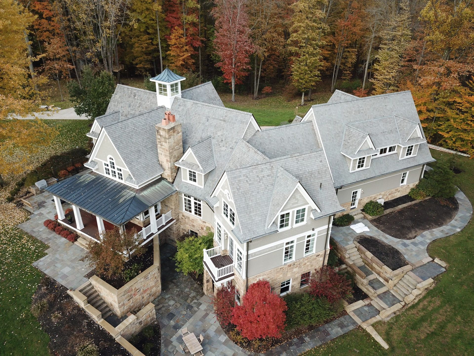 Large gray house with white trim and a covered porch, surrounded by autumn trees.