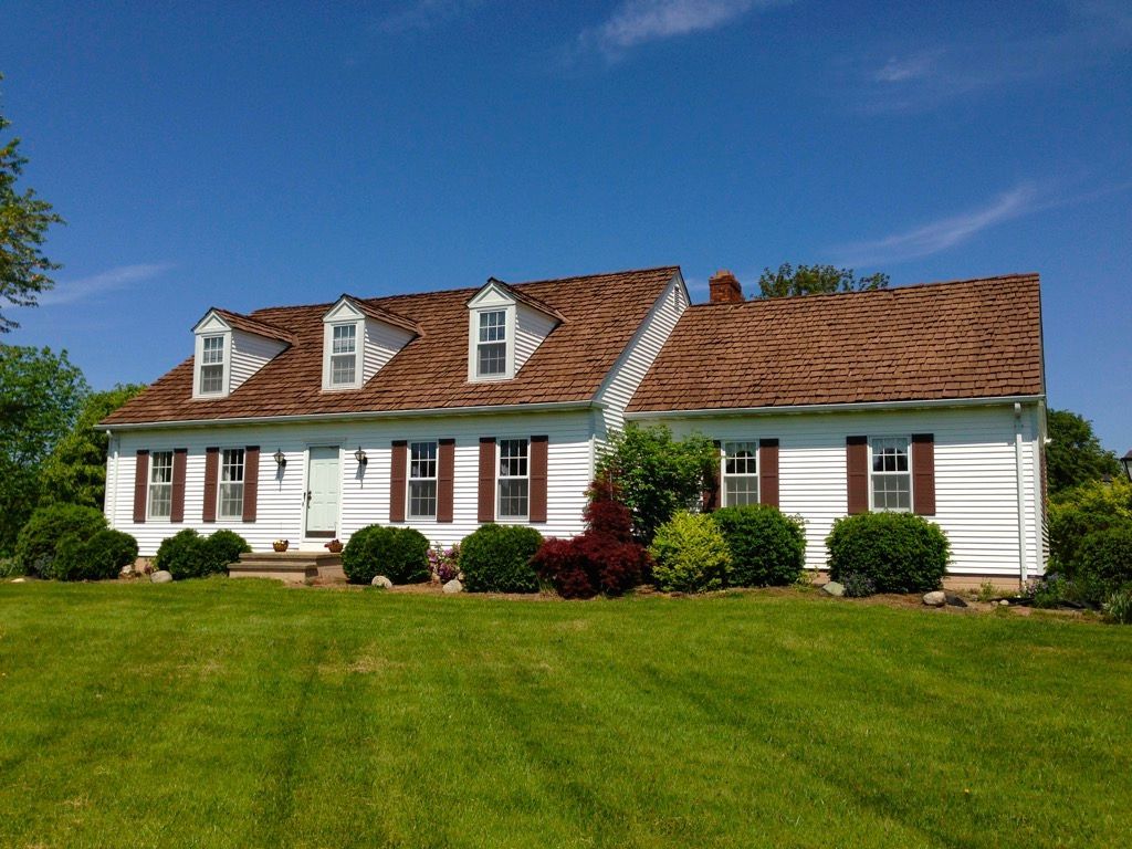 White house with red roof and dormer windows on a green lawn under a clear blue sky
