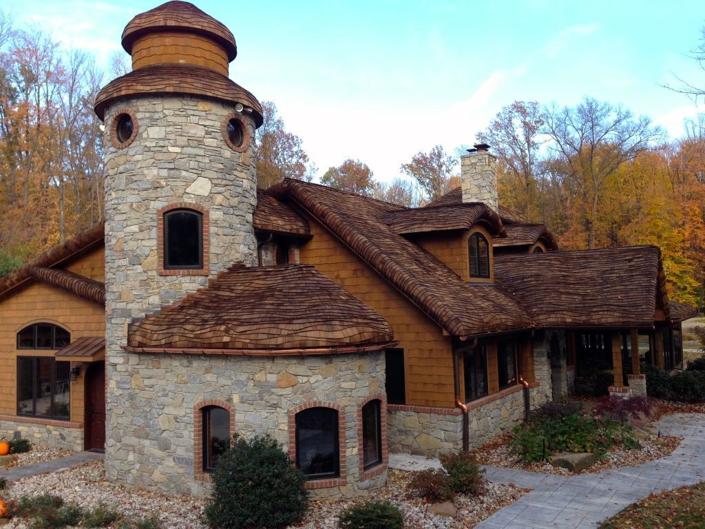 Stone house with a round tower and shingled roof, set among autumn trees.