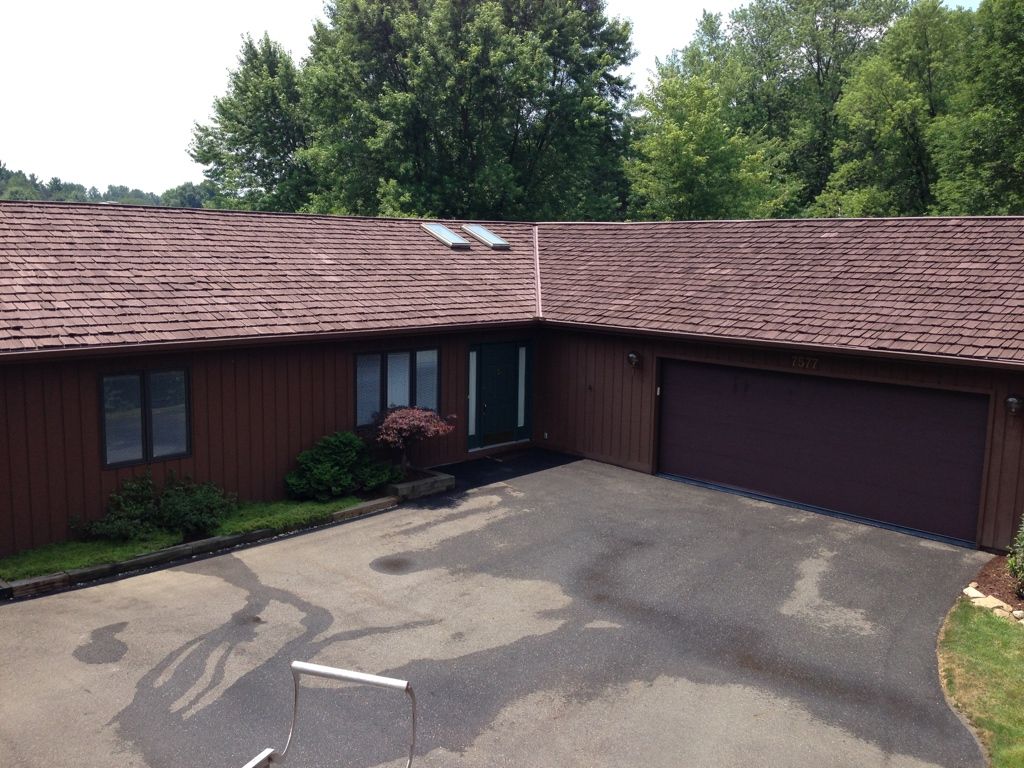 Single-story house with brown roof, garage, and driveway under trees