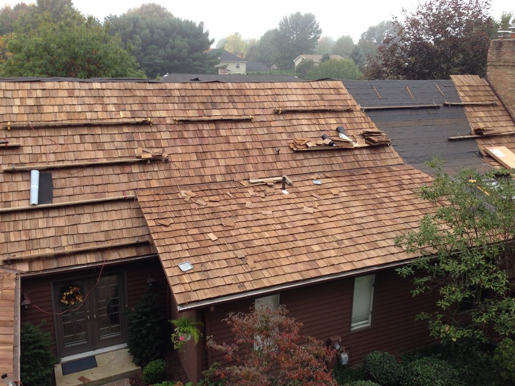 Severely damaged brown shingle roof with missing sections and visible tarps on a house