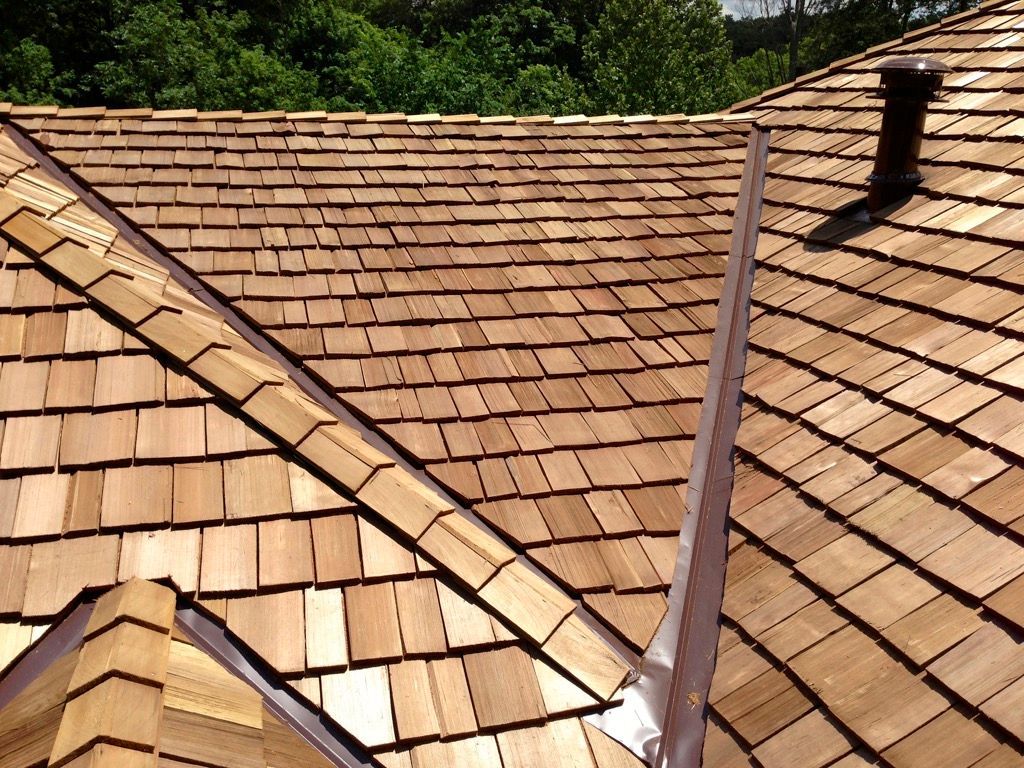 Weathered tan shingle roof with two valleys and green trees in the background