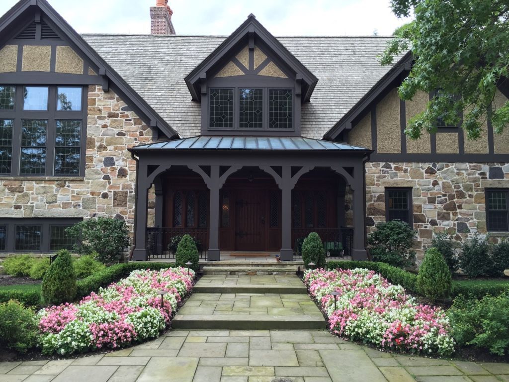 Stone house with dark timber accents, flower-lined path, and covered front porch