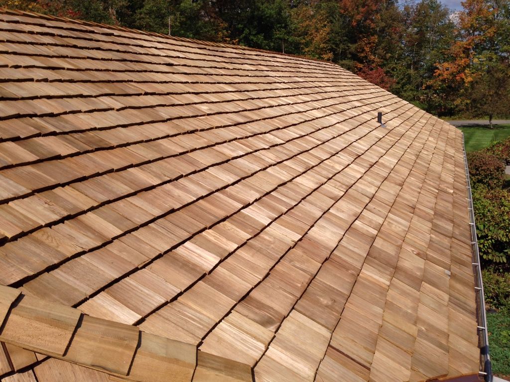Brown shingled roof with a steep slope, viewed from above against trees in the background