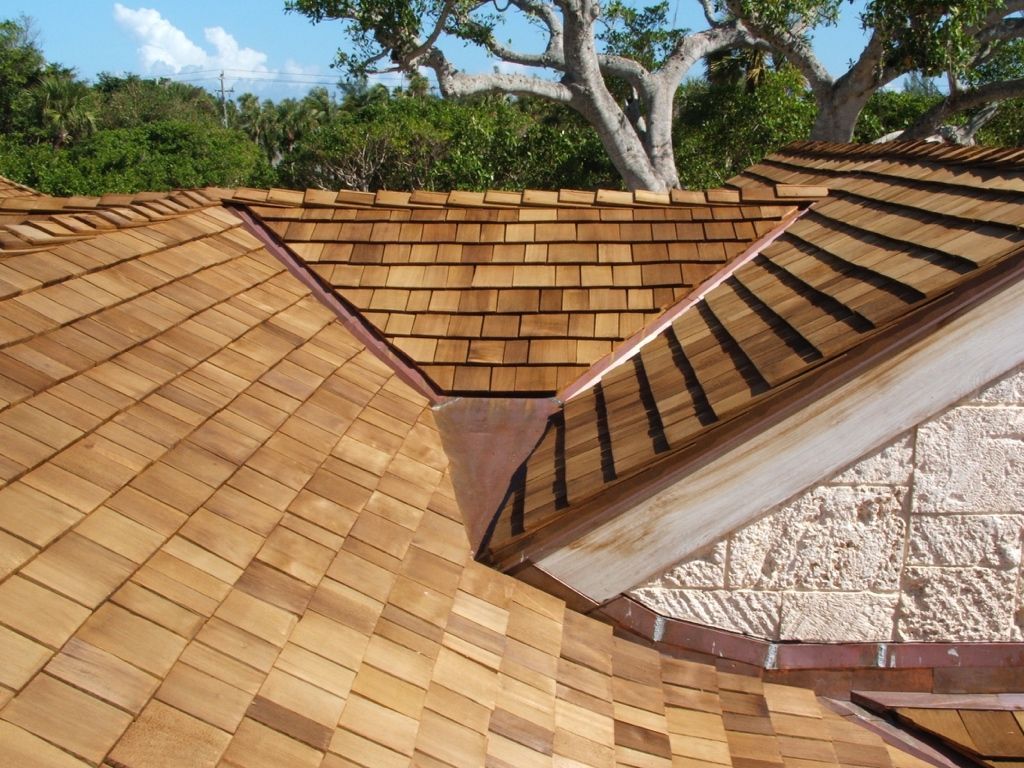 Tiled roof with intersecting ridges and valleys, set against trees and blue sky