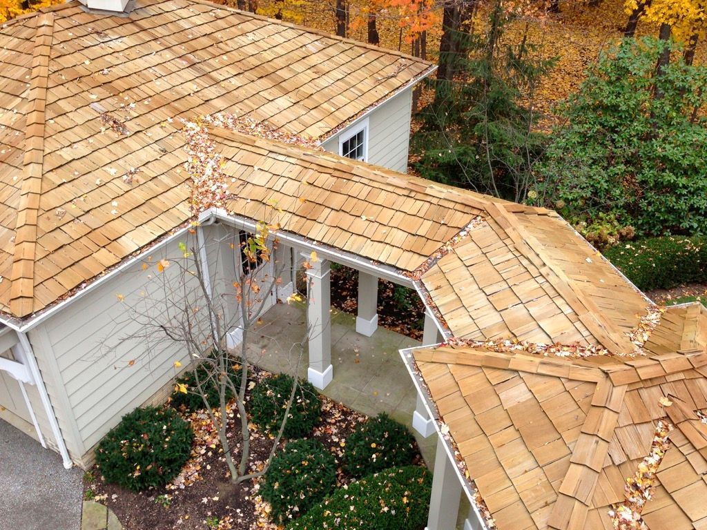 Aerial view of a tan-roofed house with a covered front entry and surrounding trees.