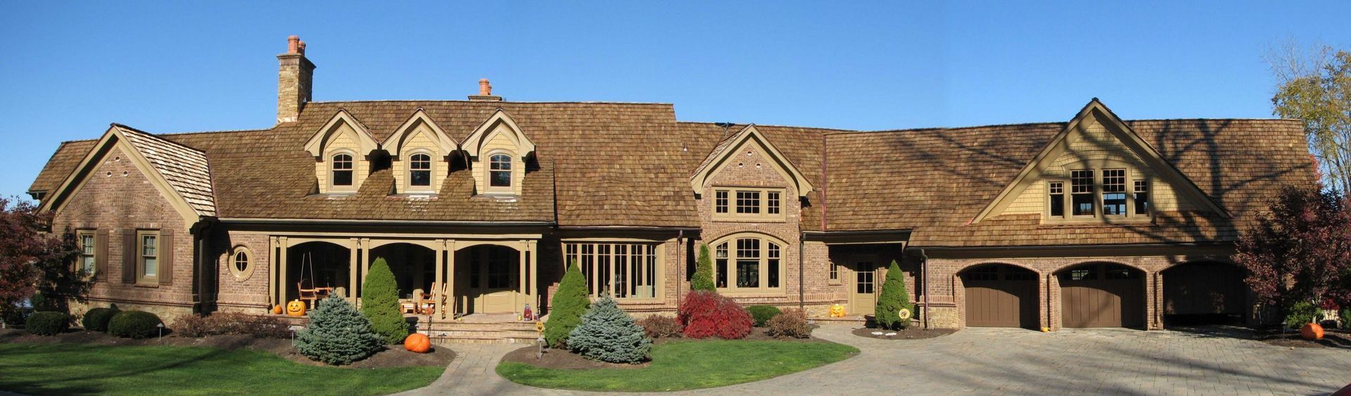 Large stone house with gabled roof, arched porch, and manicured garden under a clear blue sky