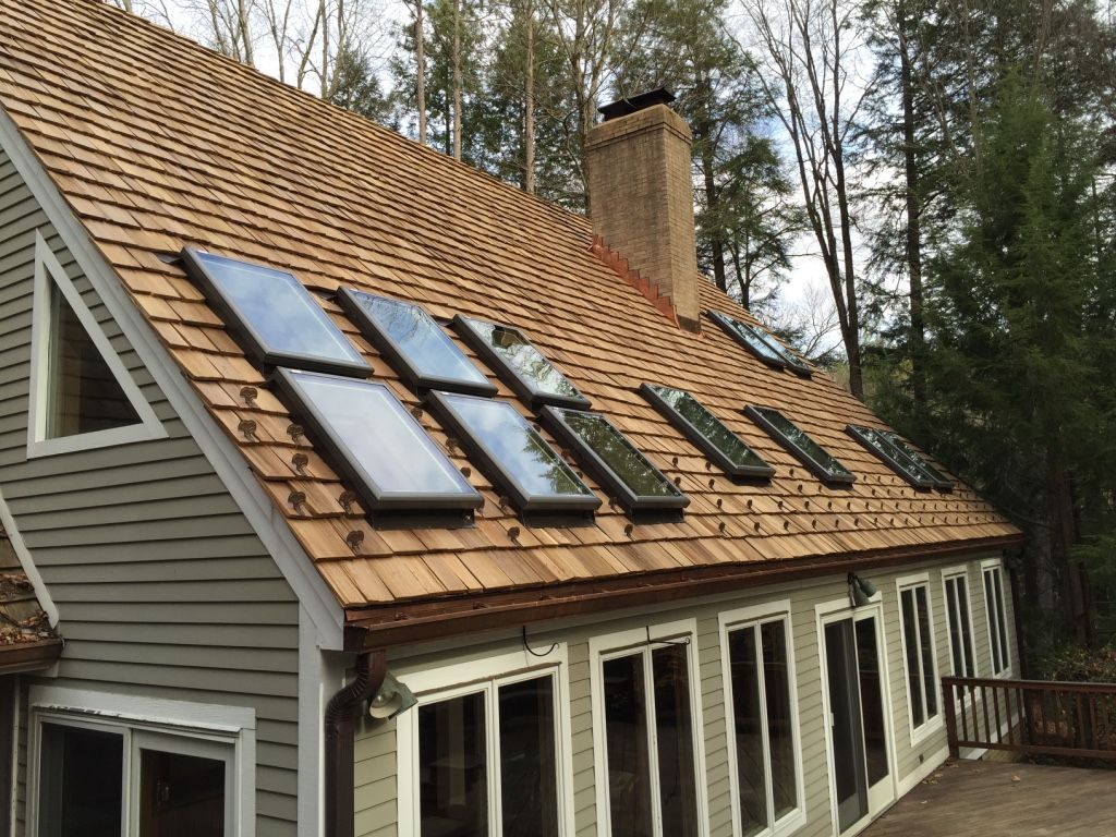 Wooden house roof with several solar panels and skylights amid trees