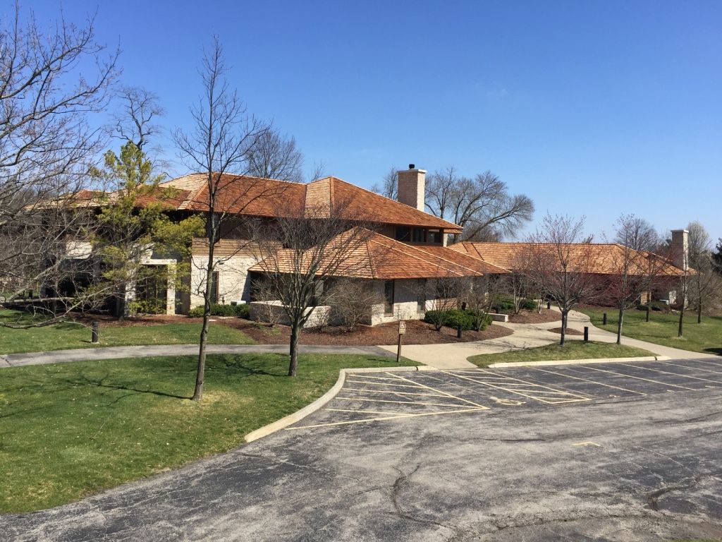 Single-story building with orange roof, trees, and a parking lot under a clear blue sky