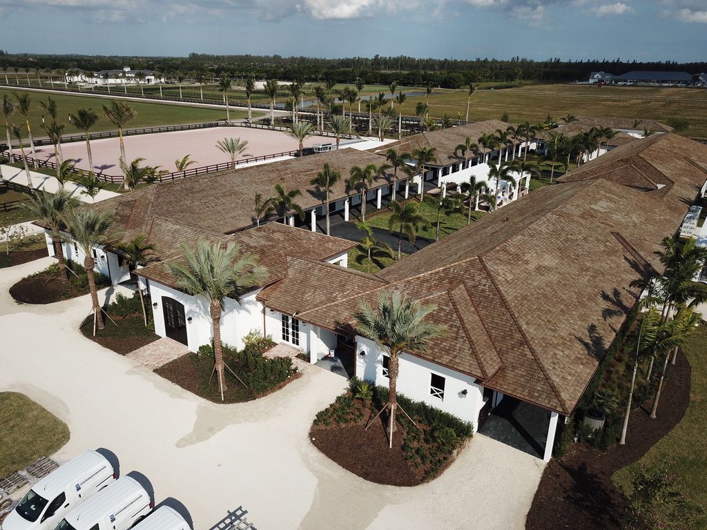 Aerial view of white resort buildings with thatched roofs, palm trees, and parked cars under a clear sky