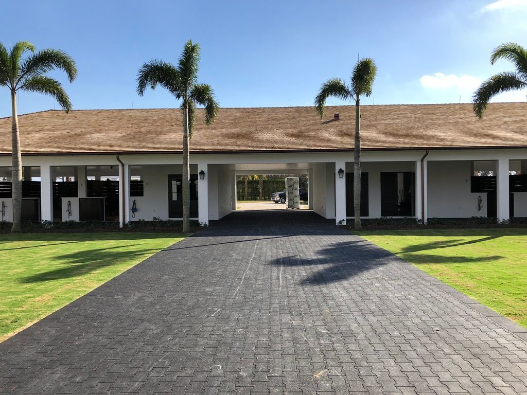 Covered walkway to a white building with palm trees and a cobblestone path under a clear sky