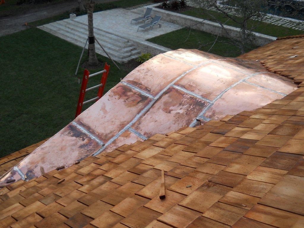 Damaged copper roof panel being lifted onto a shingled roof by a crane