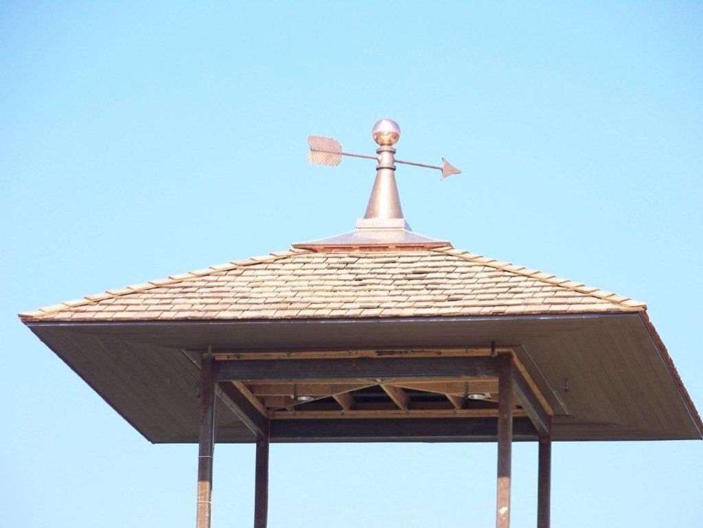 Weather vane atop a shingled pavilion roof against a clear blue sky