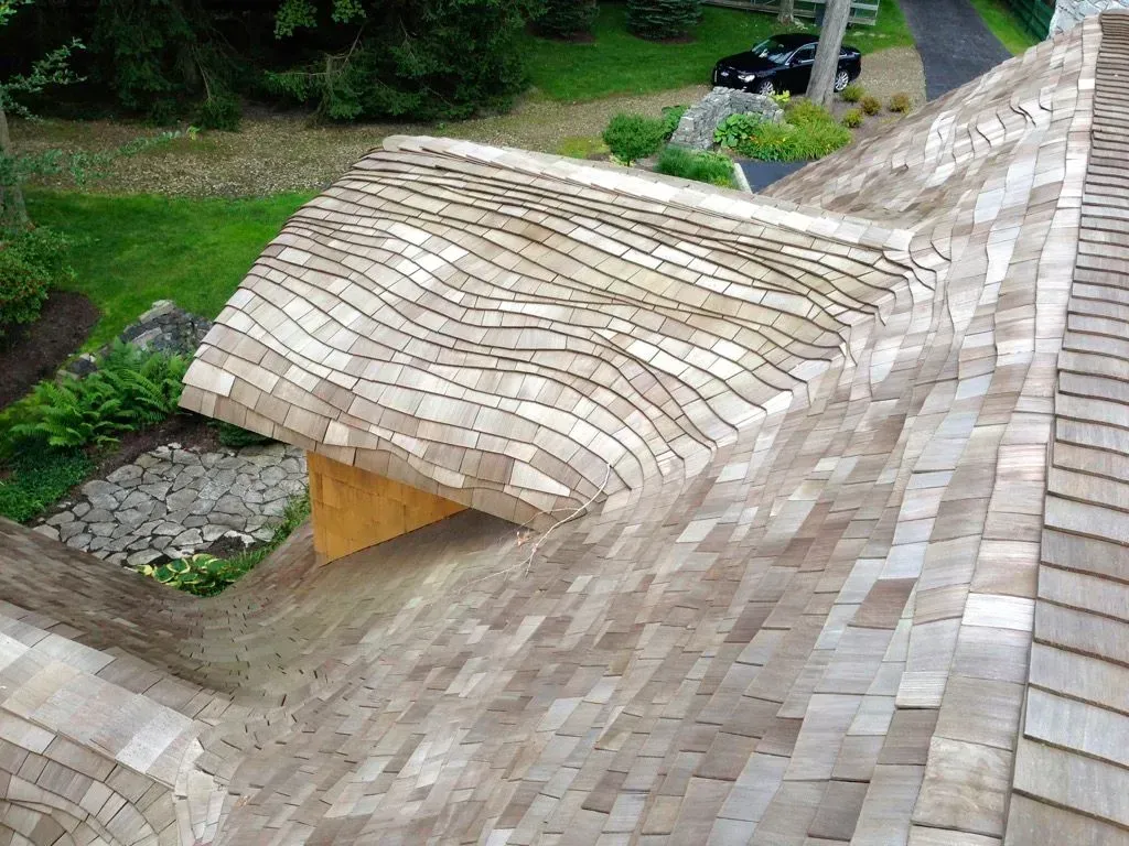 Curved shingled roof over a grassy courtyard with trees and a walkway nearby