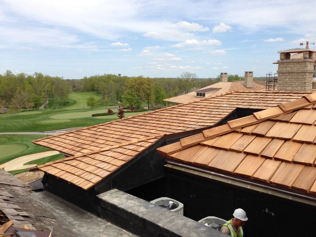 Terracotta roof tiles on a building with a person in a hard hat below, beside a green landscape