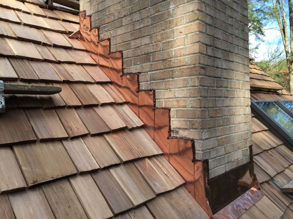 Damaged shingled roof with a brick chimney and rust-colored flashing at the seam