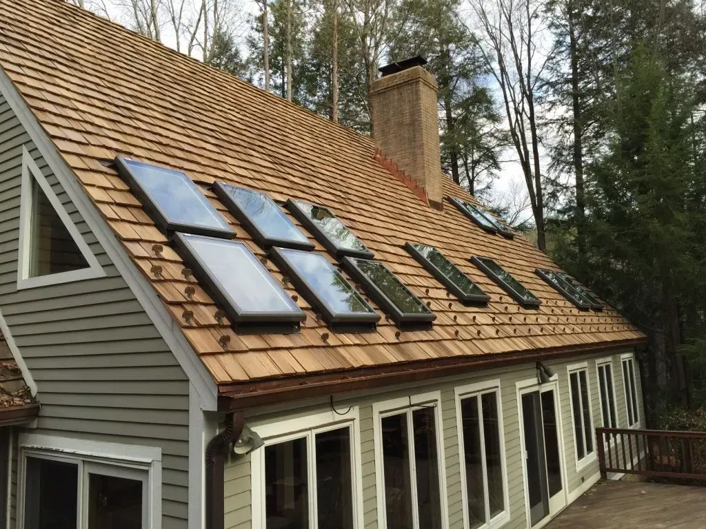 House roof with multiple solar panels beside a chimney, surrounded by trees