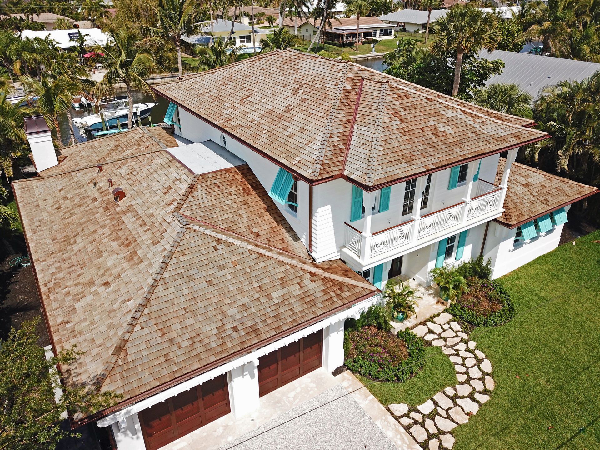 Aerial view of a white tropical house with red-tiled roofs, green lawn, and stone walkway