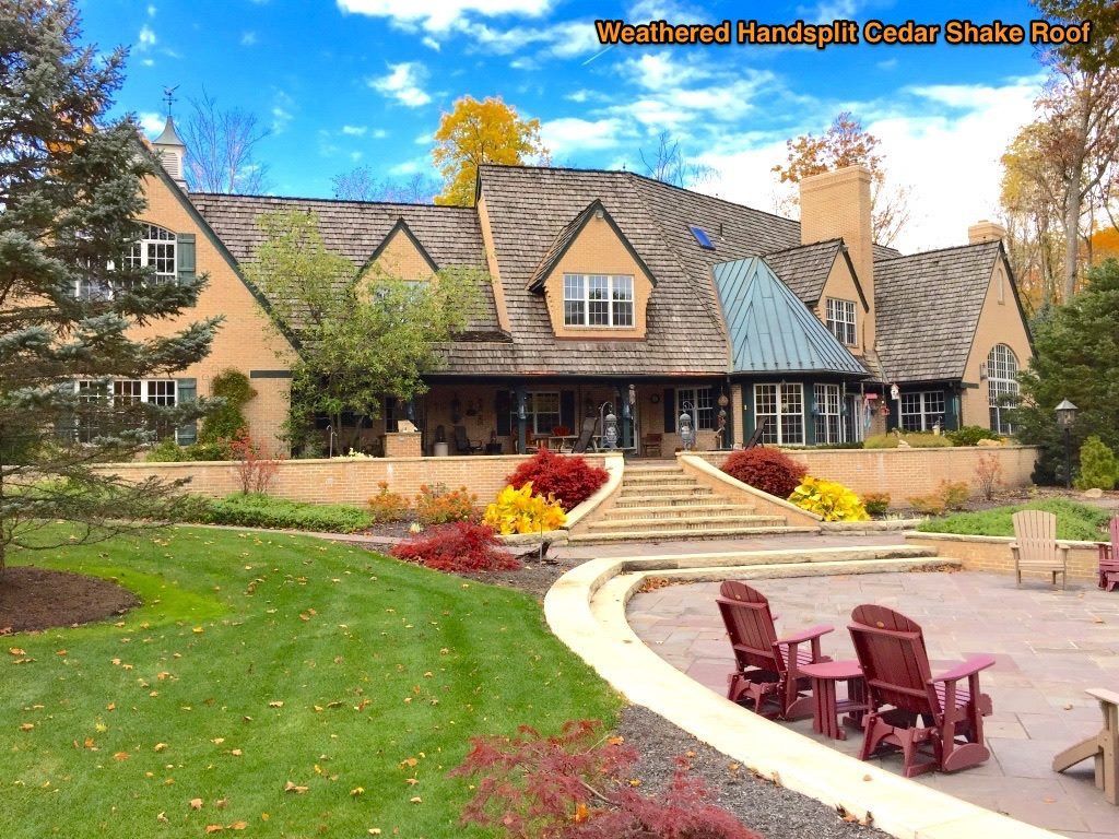 Large stone house with steep roof, autumn trees, and red chairs around a curved patio path.